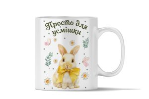 Біла керамічна чашка з акварельним малюнком пухнастого зайця з жовтим бантом, оточеного ромашками, та написом зеленого кольору «Просто для усмішки».